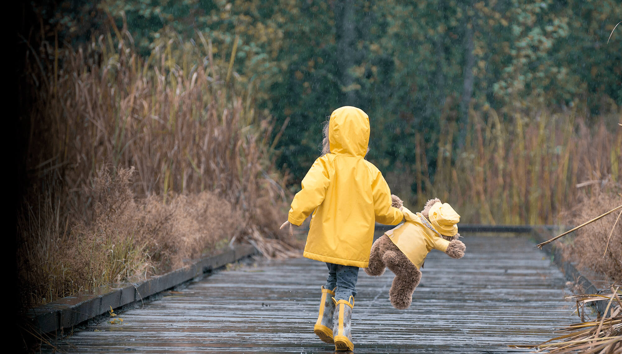 copil în impermeabil galben cu ursuleț de jucărie