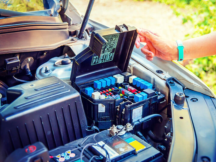 Someone opening fuse control box with relays under the hood of a car